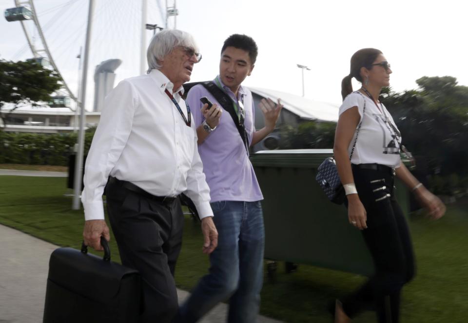 Formula One Chief Executive Bernie Ecclestone (L) and his wife Fabiana Flosi (R) walk with an unidentified man ahead of the third practice session of the Singapore F1 Grand Prix at the Marina Bay street circuit in Singapore September 21, 2013. REUTERS/Pablo Sanchez (SINGAPORE - Tags: SPORT MOTORSPORT F1)