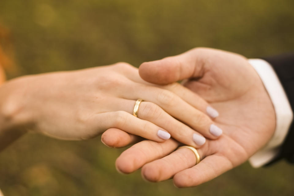 A women's hand wearing a ring, holding a man's hand with a ring, presumably on their wedding day.