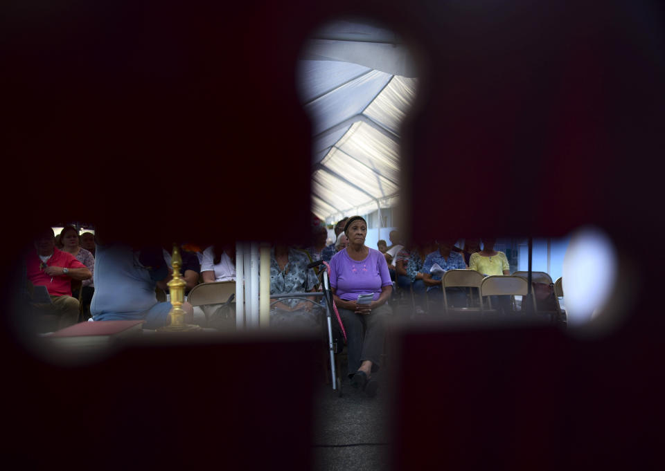 Seen through the cut-out shape of a cross on a priest's chair, a woman attends an outdoor Mass under a tent set up near the Immaculate Concepcion Catholic Church, which sustained earthquake-related damaged earlier in the week, following a magnitude 5.9 quake earlier in the day in Guanica, Puerto Rico, Saturday, Jan. 11, 2020. The morning quake caused further damage along the island’s southern coast, where previous recent quakes have toppled homes and schools. (AP Photo/Carlos Giusti)