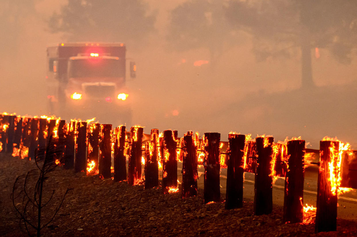 A fire engine drives past flaming highway guard rails. (Josh Edelson / AFP via Getty Images)