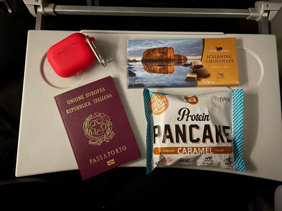 A red airpods case, Italian passport, Icelandic chocolate bar, and protein pancake on a seat tray Asia London Palomba PLAY Airlines review