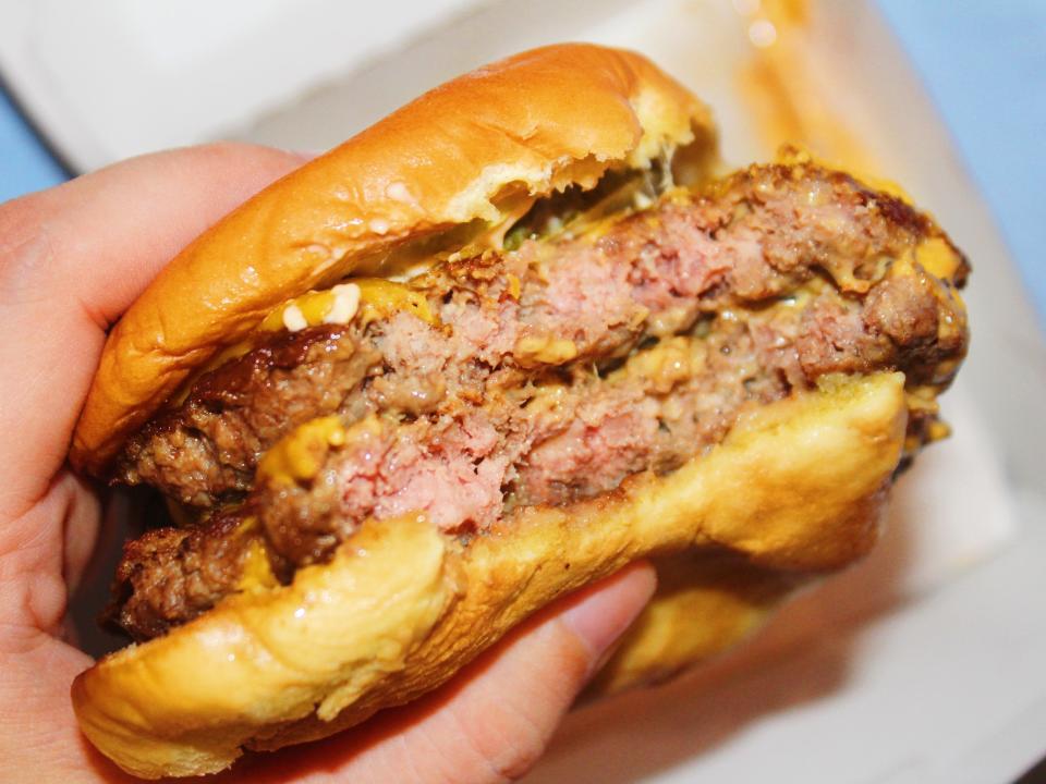 bitten into shake shack double cheeseburger in paper wrapping on blue background