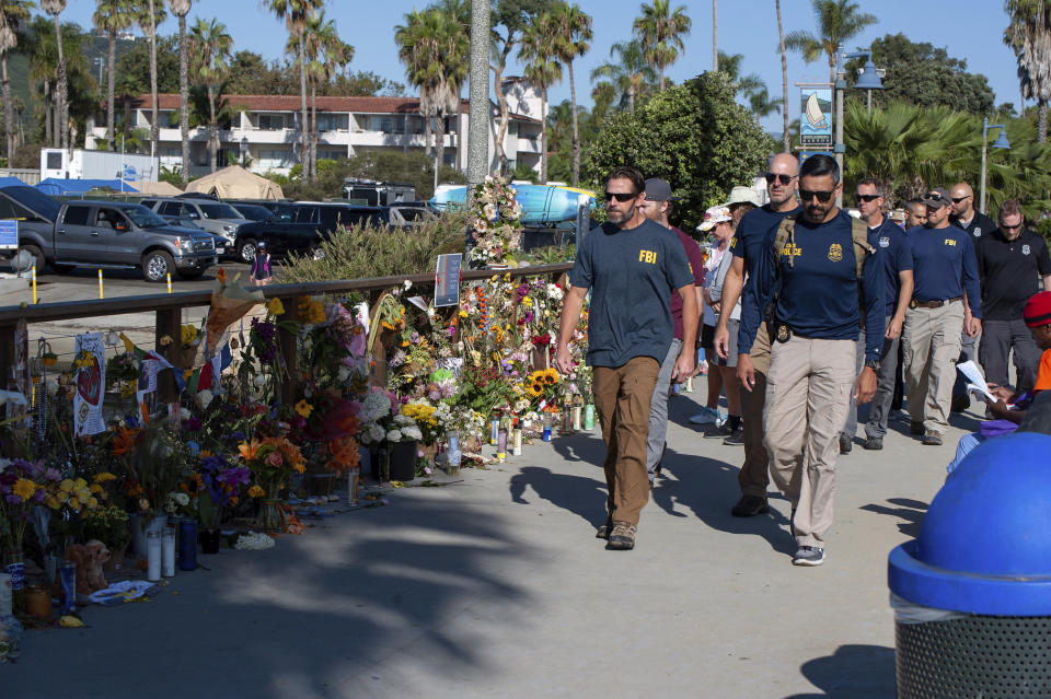 FBI agents walk past a memorial for the victims of the Conception dive boat on the Santa Barbara Harbor, as authorities issue a search warrant for the Truth Aquatics' offices in Santa Barbara, Calif., Sunday, Sept. 8, 2019. The office was ringed in red "crime scene" tape as more than a dozen agents took photos and carried out boxes. Thirty-four people died when the Conception burned and sank before dawn on Sept. 2. They were sleeping in a cramped bunkroom below the main deck and their escape routes were blocked by fire. (AP Photo/Christian Monterrosa)