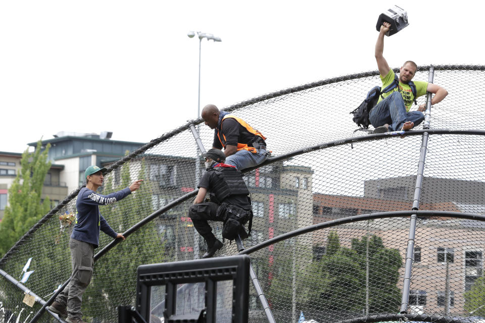 Two street preachers, at right and left, are kept separated by people volunteering in the Capitol Hill Occupied Protest zone after they climbed a baseball backstop at Cal Anderson Park, Saturday, June 20, 2020, in Seattle. The two men clashed with protesters and others throughout the day as they yelled homophobic slurs, played loud music, and shouted sermons. The conflict was in addition to tensions from a pre-dawn shooting near the area that left one person dead and critically injured another person. The area has been occupied by protesters after Seattle Police pulled back from several blocks of the city's Capitol Hill neighborhood near the Police Department's East Precinct building. (AP Photo/Ted S. Warren)