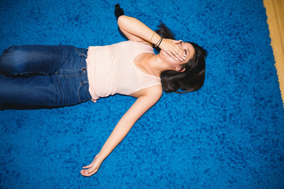Young woman wearing blue jeans and a pink tank top lying on her back on the floor laughing with a hand over her mouth