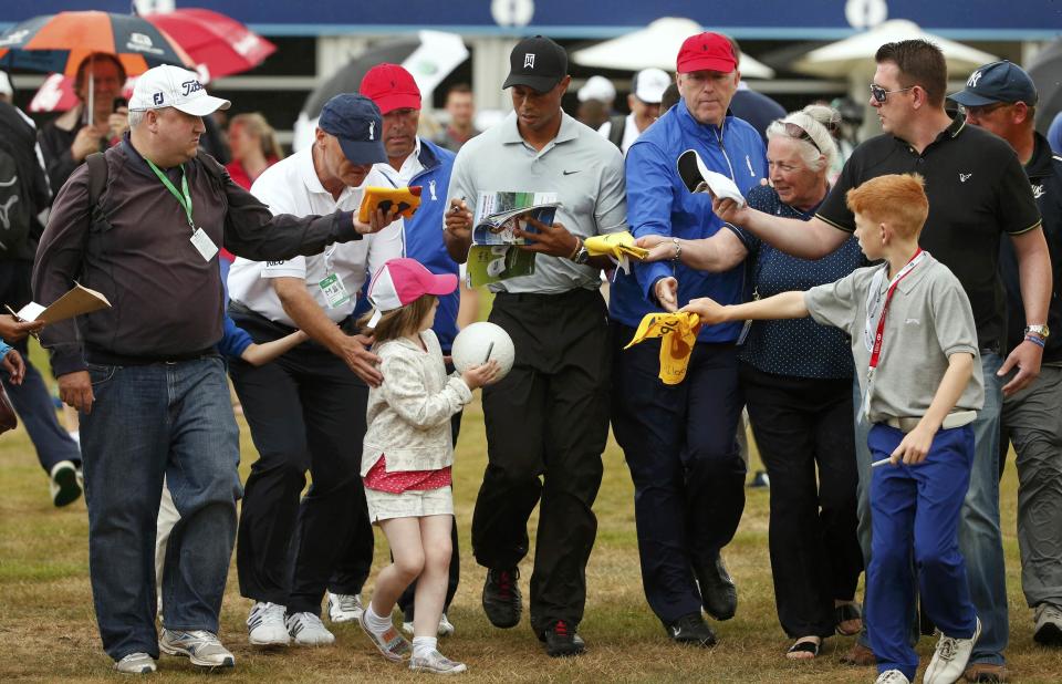 Tiger Woods of the U.S. signs autographs for fans as he walks back to the clubhouse after a practice round ahead of the British Open Championship at the Royal Liverpool Golf Club in Hoylake, northern England July 16, 2014. REUTERS/Cathal McNaughton (BRITAIN - Tags: SPORT GOLF)