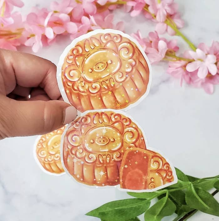 Hand holding glistening mooncake stickers with pig design.