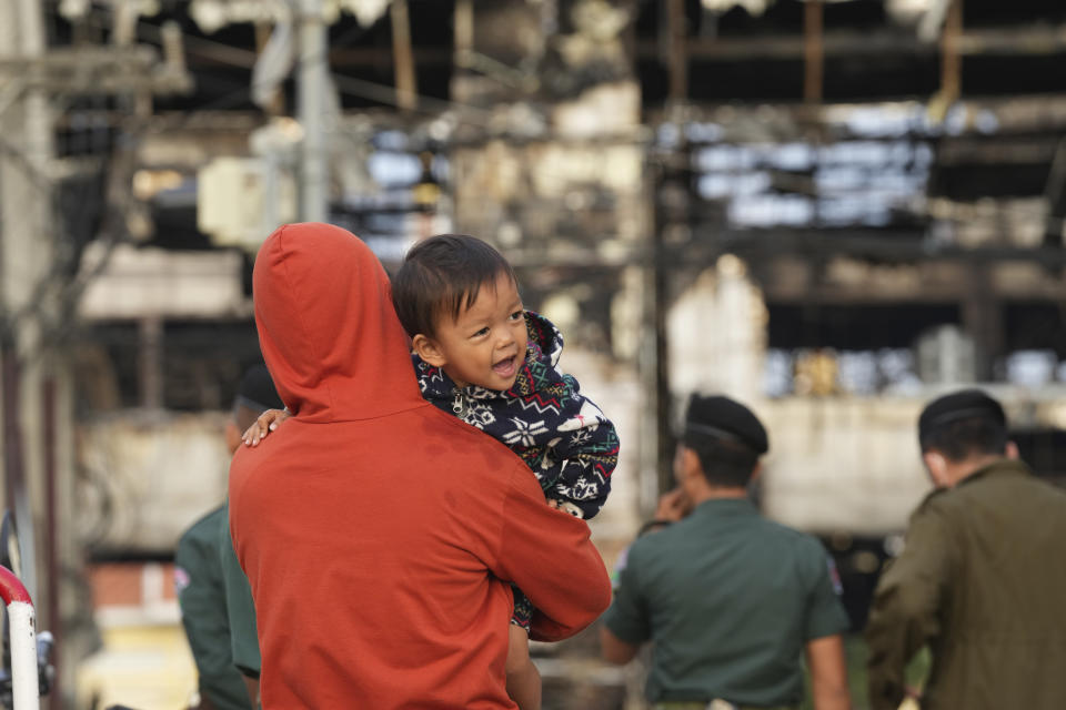 A man holds his child as he watches a ruined building at the scene of a massive fire at a Cambodian hotel casino in Poipet, west of Phnom Penh, Cambodia, Friday, Dec. 30, 2022. The fire at the Grand Diamond City casino and hotel Thursday injured over 60 people and killed more than a dozen, a number that officials warned would rise after the search for bodies resumes Friday. (AP Photo/Heng Sinith)