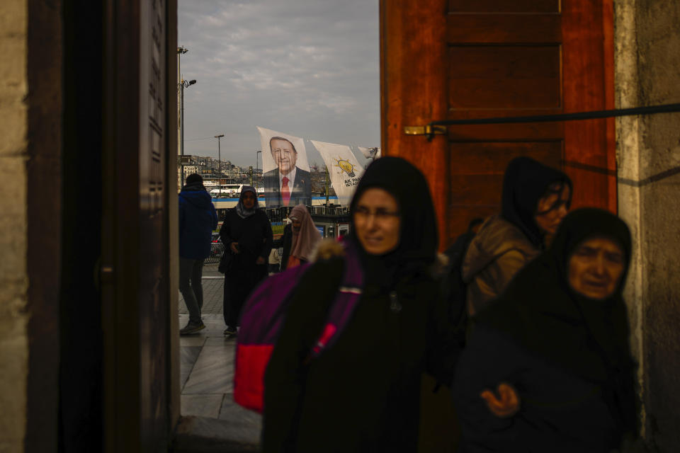 People step in Yeni Camii or New Mosque next to a campaign banner of Turkish President and leader of the Justice and Development Party, or AKP, Recep Tayyip Erdogan, in Istanbul, Turkey, Saturday, March 16, 2024. On Sunday, millions of voters in Turkey head to the polls to elect mayors and administrators in local elections which will gauge President Recep Tayyip Erdogan’s popularity as his ruling party tries to win back key cities it lost five years ago. (AP Photo/Emrah Gurel)