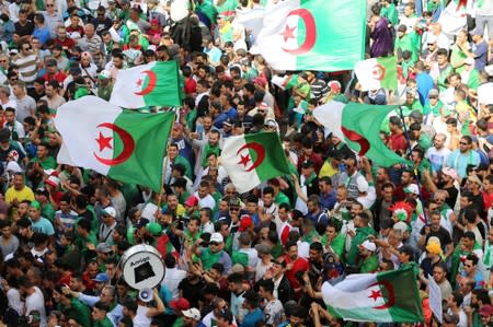 Demonstrators gesture and carry flags during a protest demanding the removal of the ruling elite in Algiers