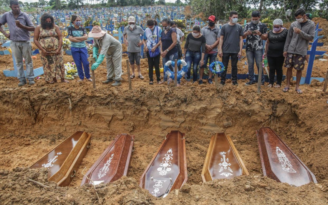 People wearing protective masks observe to the graves with the remains of their relatives during a mass burial of coronavirus victims - Getty Images South America 