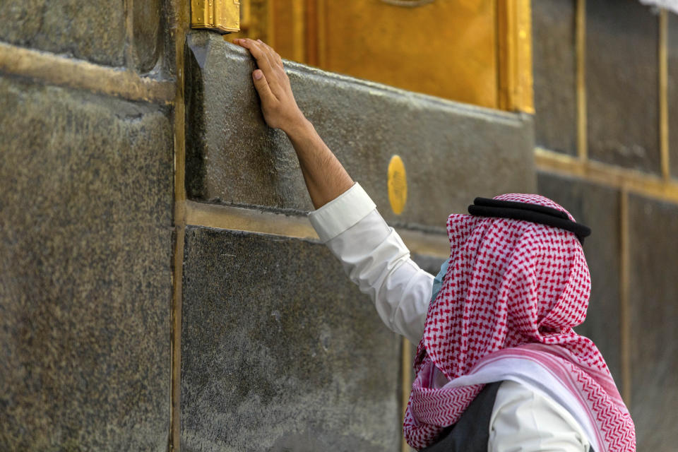 A pilgrim touches the Kaaba, the square structure in the Great Mosque, toward which believers turn when praying, in Mecca, Saudi Arabia, Monday, July 27, 2020. Anywhere from 1,000 to 10,000 pilgrims will be allowed to perform the annual hajj pilgrimage this year due to the coronavirus pandemic. (Saudi Ministry of Media via AP)