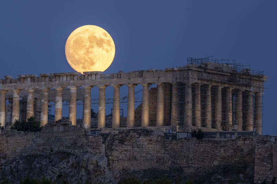 The moon rises in the sky behind the 5th century B.C. Parthenon temple at the ancient Acropolis hill, in Athens, on Monday, July 31, 2023. (AP Photo/Petros Giannakouris)