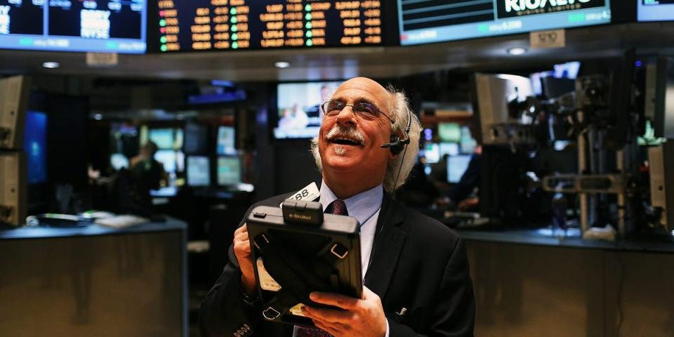 A trader on the New York Stock exchange smiles while looking up from a screen.