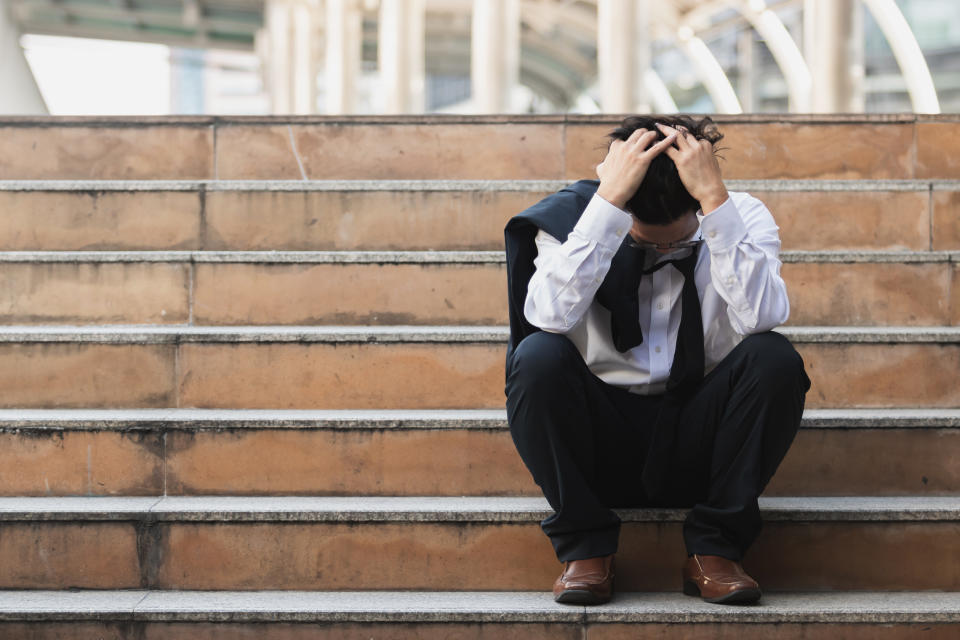 Upset stressed young business man in suit with hands on head sitting on stairs. Unemployment and layoff concept.