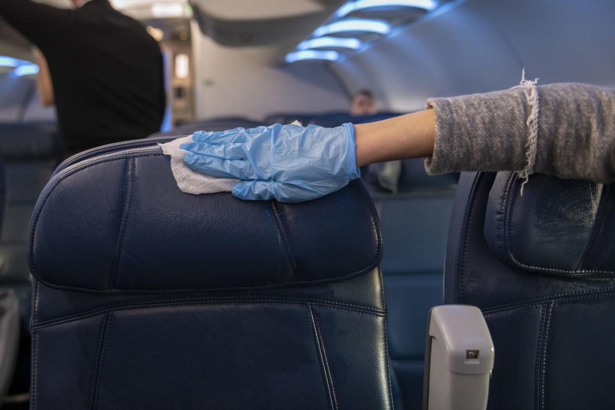 A passenger who has just boarded an airplane wears a plastic glove while using a wipe to disinfect the airplane seats and armrests on her row.