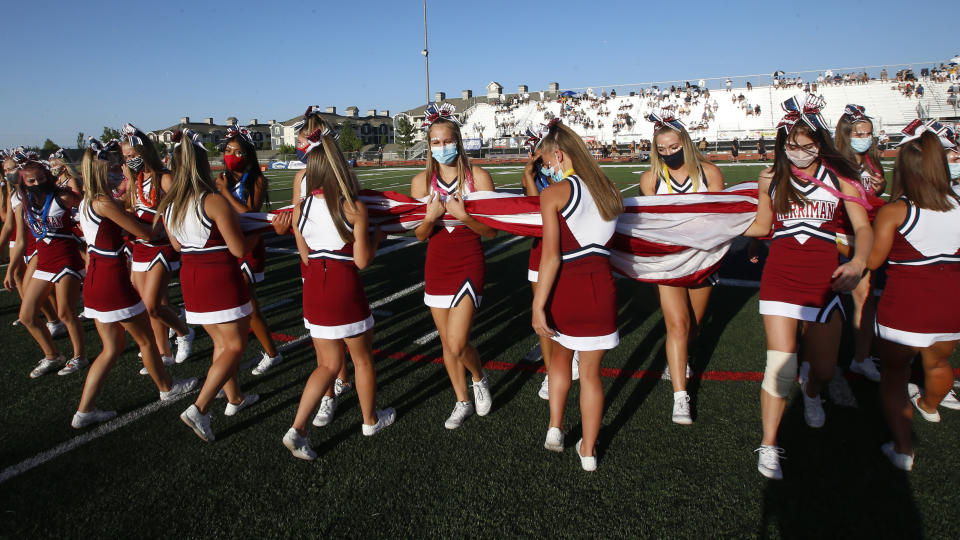 Herriman cheerleaders carry the American flag before the start of a high school football game between Davis and Herriman on Thursday, Aug. 13, 2020, in Herriman, Utah. Utah is among the states going forward with high school football this fall despite concerns about the ongoing COVID-19 pandemic that led other states and many college football conferences to postpone games in hopes of instead playing in the spring. (AP Photo/Rick Bowmer)