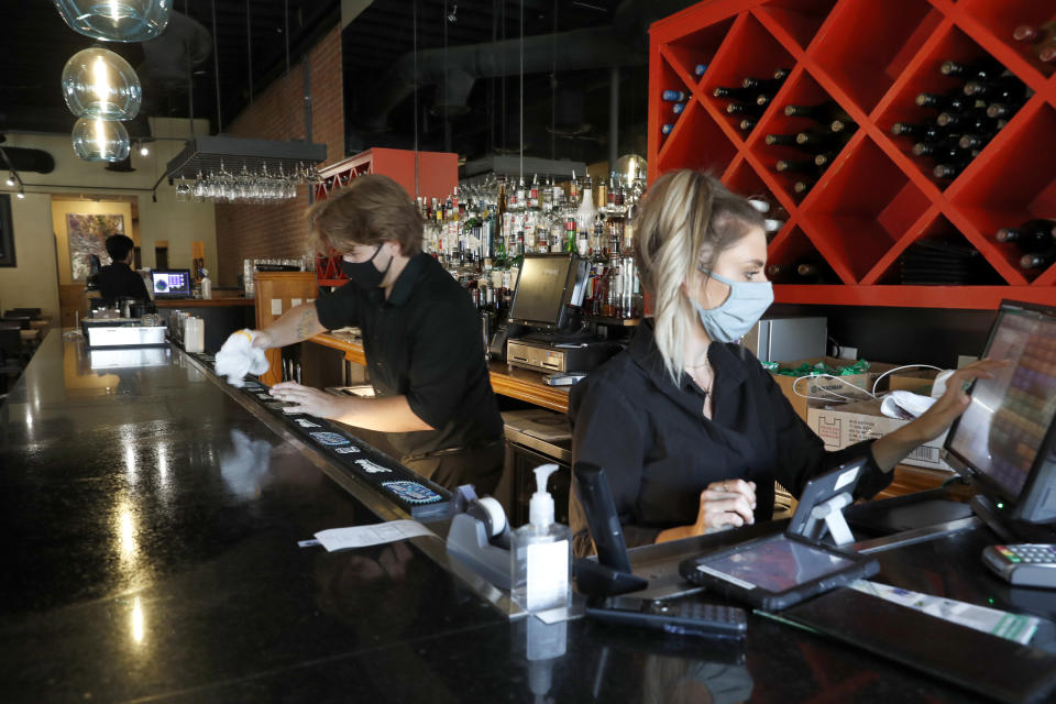 Deep Sushi restaurant employees Jordan Arrowood, left, cleans the bar top as Carrie Souza enters an order at the sushi restaurant in the Deep Ellum entertainment district in Dallas, Friday, June 26, 2020. Texas Gov. Greg Abbott announced Friday that he is shutting bars back down and scaling back restaurant capacity to 50%, in response to the increasing number of COVID-19 cases in the state. (AP Photo/Tony Gutierrez)