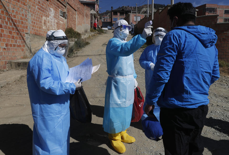 Un médico vestido con equipo de protección completo mide la temperatura de un hombre durante una prueba de detección de coronavirus de casa en casa en Villa El Rosal, en las afueras de La Paz, Bolivia, el domingo 12 de julio de 2020. (AP Foto/Juan Karita)