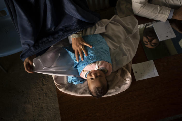 A baby lies on the doctor's desk before being examined at the hospital in Mirbacha Kot, Afghanistan, Monday, Oct. 25, 2021. Health care workers continue to work without salaries, without medicine and with frequent power cuts as Afghanistan's economy crumbles. (AP Photo/Bram Janssen)