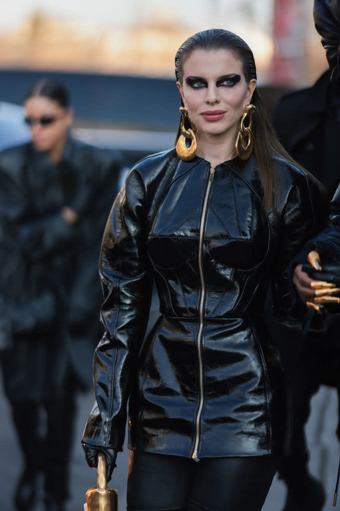 With dramatic eye makeup, door-knocker earrings, and long-sleeved leather minidress jacket with long front zipper