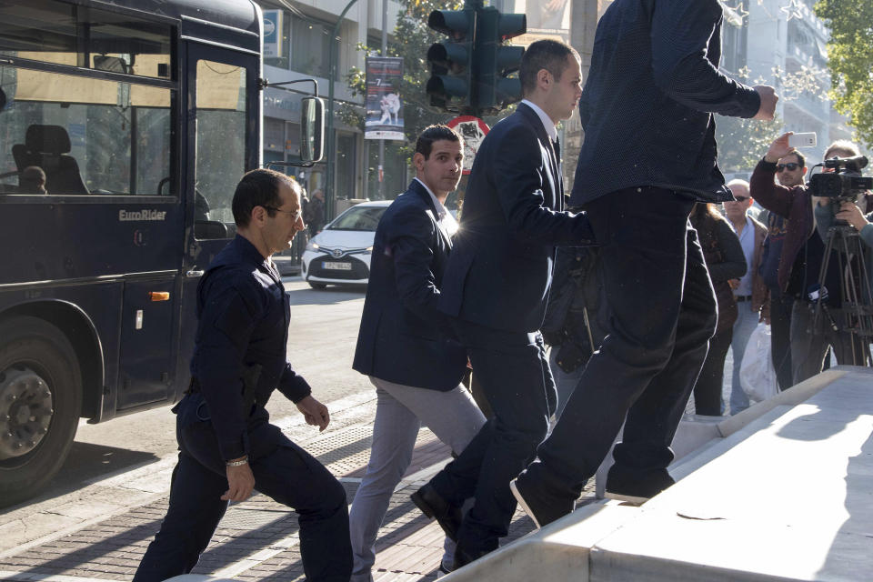 A Greek police officer escorts three of nine suspects in the fatal beating of an American tourist in an island resort last year, at a court house in Patras, western Greece, on Thursday, Nov. 22, 2018. A Greek court on Thursday convicted and sentenced six of nine suspects in the fatal beating of an American tourist in an island resort last year. Bakari Henderson, a 22-year-old of Austin, Texas, died after being beaten in the street following an argument in a bar in the popular Laganas resort area of Zakynthos island in July 2017. (AP Photo/Giannis Androutsopoulos)