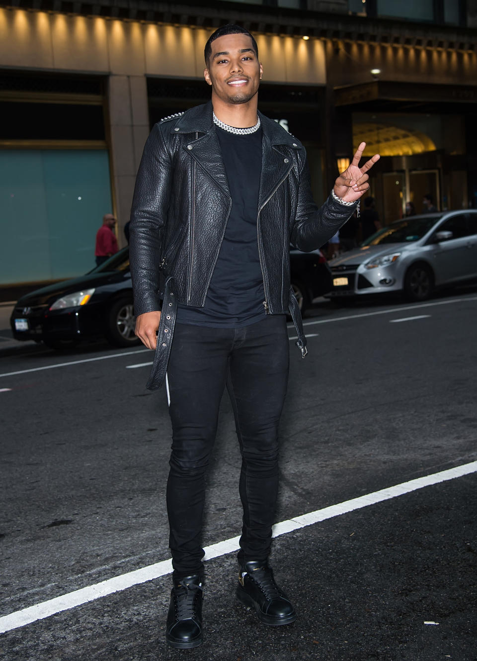 Rome Flynn poses in the middle of the street while holding up a peace sign with his hands.