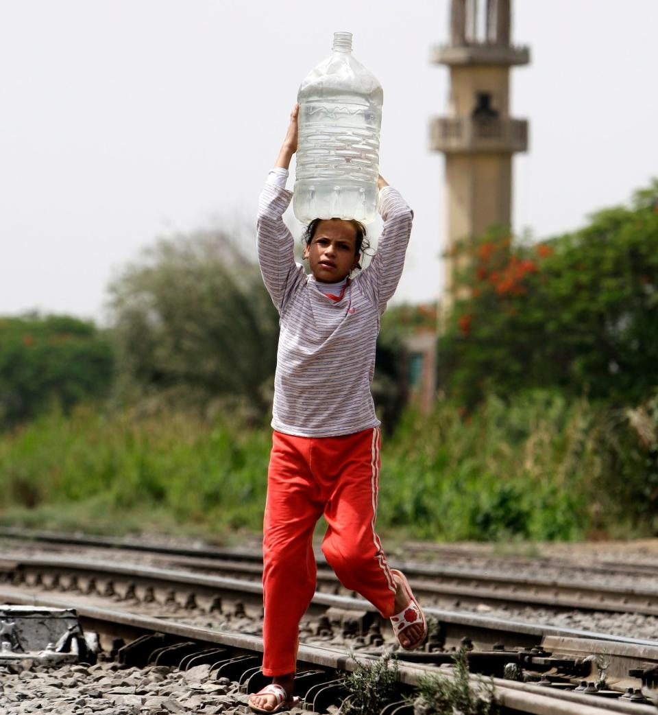A girl carries a container of water over railroad tracks