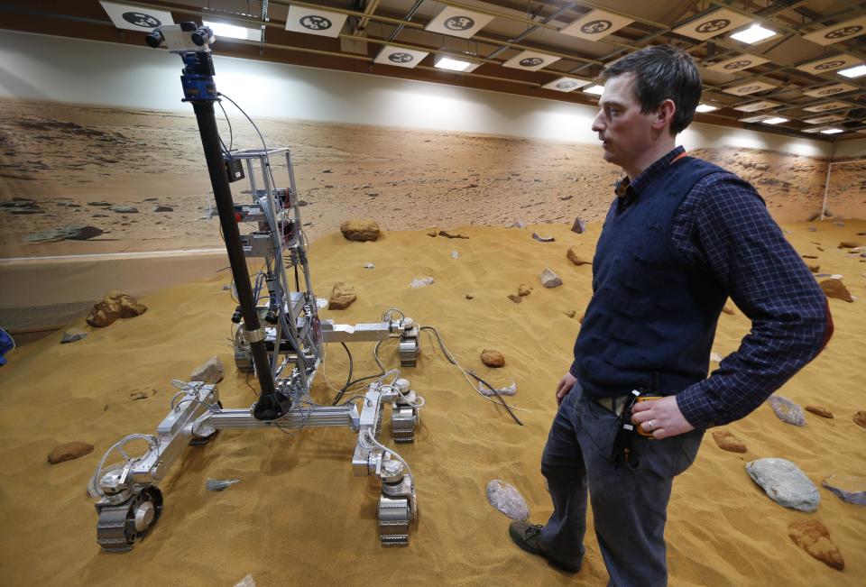 Engineer Ben Nye stands next to a robotic vehicle on the 'Mars Yard Test Area', a testing ground for the robotic vehicles of the European Space Agency’s ExoMars program scheduled for 2018, in Stevenage, England, Thursday, March 27, 2014. It looks like a giant sandbox - except the sand has a reddish tint and the “toys” on display are very expensive prototypes designed to withstand the rigors of landing on Mars. The scientists here work on the development of the autonomous navigation capabilities of the vehicle, so by being in communication with controllers on earth twice a day, will be able to use the transmitted information to navigate to new destinations on Mars. (AP Photo/Lefteris Pitarakis)