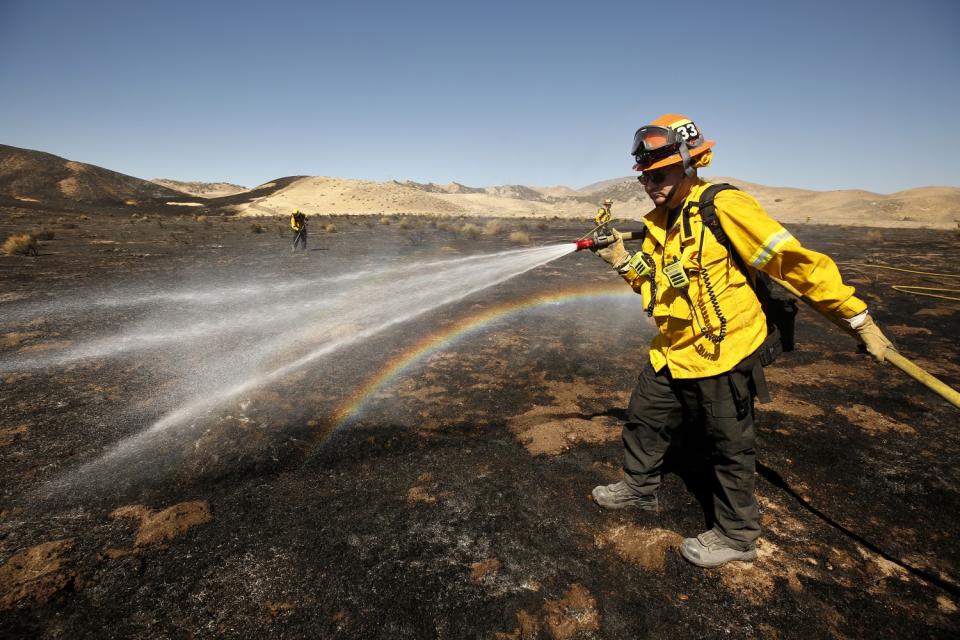 Water from a firefighter's hose creates a rainbow in a burned area