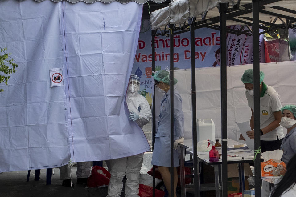 In this Thursday, March 19, 2020, photo, a health officer in a Hazmat suite talks with a nurse at a makeshift screening facility outside Rajadamnern boxing stadium in Bangkok, Thailand. Kickboxing aficionados came from all over Thailand to attend a major Muay Thai tournament at Bangkok's indoor Lumpini Stadium on March 6, 2020. Dozens or more went home unknowingly carrying the coronavirus. For most people the new COVID-19 coronavirus causes only mild or moderate symptoms, but for some it can cause more severe illness. (AP Photo/Gemunu Amarasinghe)