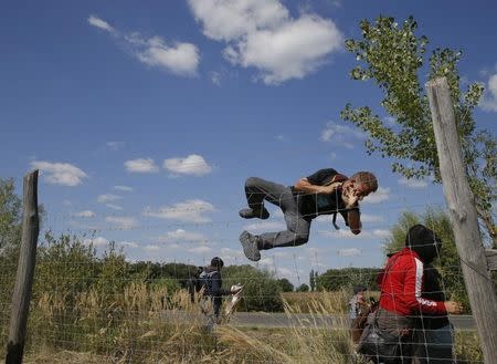 A migrant jumps over a road protection fence as they leave a collection point in the village of Roszke, Hungary September 9, 2015. REUTERS/Marko Djurica