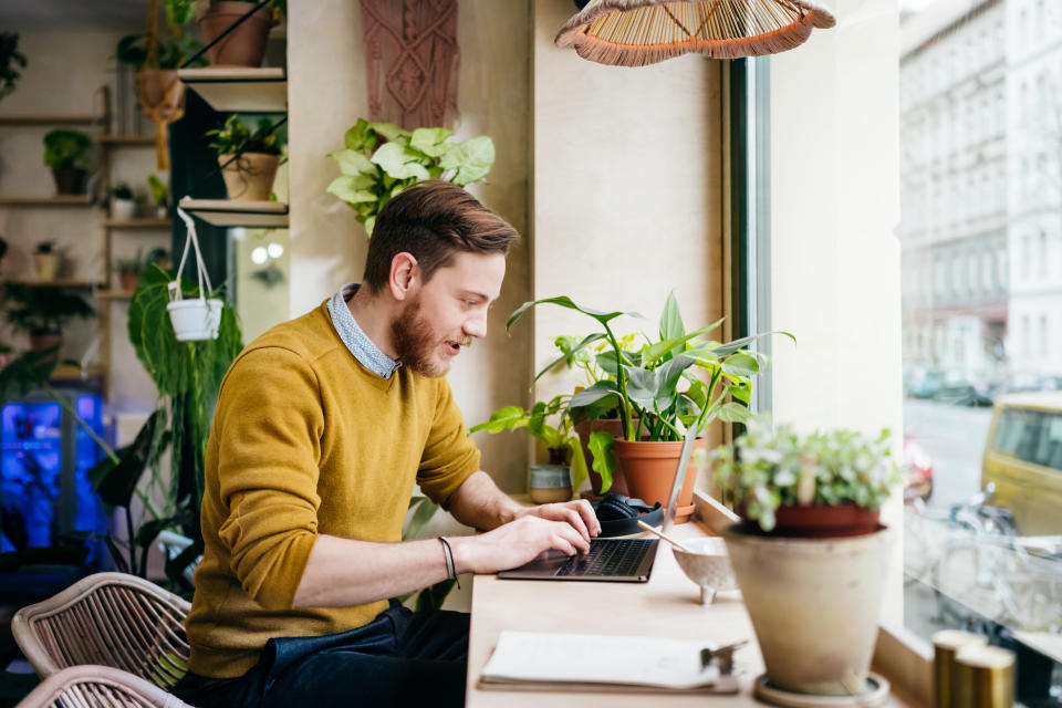 A man sitting in a small café using his laptop. (Source: Getty)