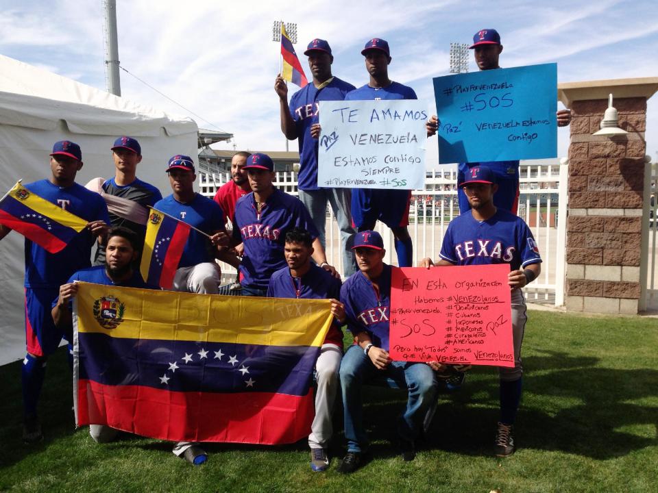 Texas Rangers baseball players pose for a photo in support of friends and family members of teammates in Venezuela including shortstop Elvis Andrus, front left, pitcher Yu Darvish, standing second from left, and third baseman Adrian Beltre, standing third from left, Saturday, Feb. 22, 2014, Surprise, Ariz. Political violence is blamed for at least eight deaths and more than 100 injuries since Feb. 12 in Venezuela, home to 63 players who were on opening day rosters at the beginning of the 2013 season. (AP Photo/Stephen Hawkins)