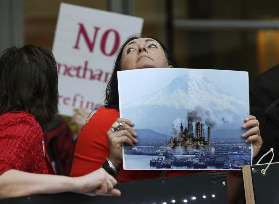 FILE - In this Feb. 10, 2016, file photo, Francesca Siena holds a photo of Mount Rainier and the Port of Tacoma that has been computer modified to include the image of a refinery as she protests in Tacoma, Wash., outside a public meeting to gather opinion on a proposed methanol plant that would be built at the Port of Tacoma. A new federal lawsuit filed Tuesday, Nov. 12, 2019, aims to kill plans to build one of the world's biggest methanol refineries along the Columbia River. (AP Photo/Ted S. Warren, File)