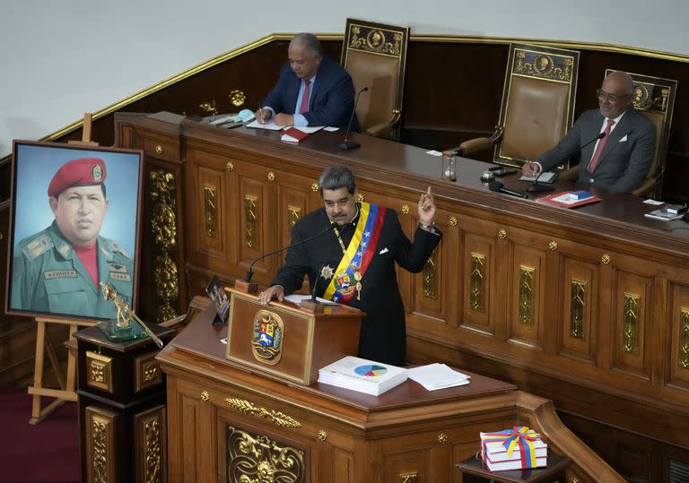 De pie junto a un retrato del fallecido expresidente Hugo Chávez, el mandatario Nicolás Maduro da su discurso anual de rendición de cuentas a la nación ante los legisladores de la Asamblea Nacional en Caracas, Venezuela, el jueves 12 de enero de 2023. (AP Foto/Ariana Cubillos)