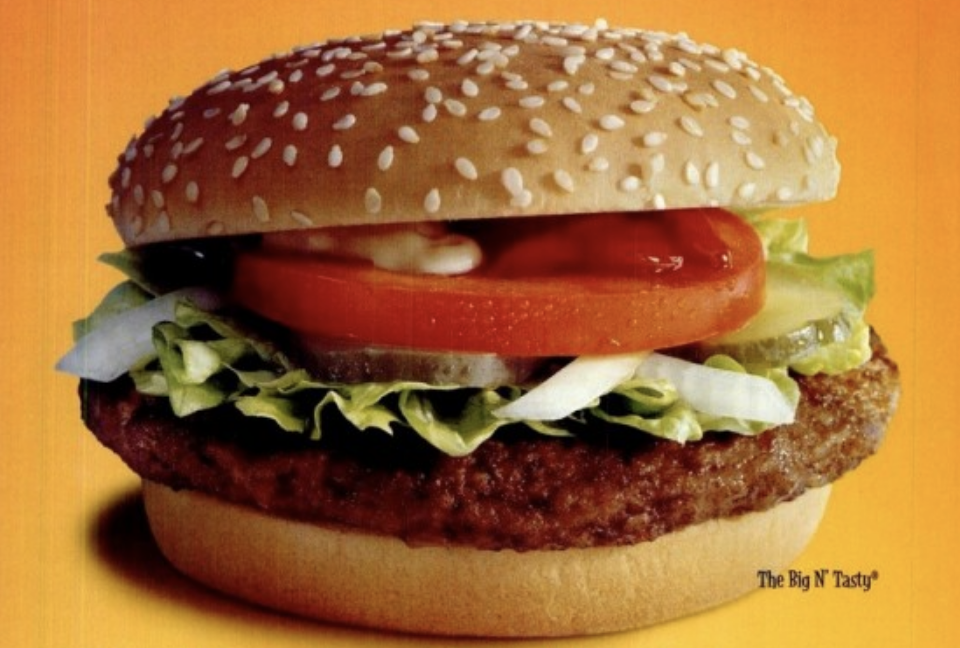 A burger with tomatoes, relish, lettuce, and onion on a sesame seed bun