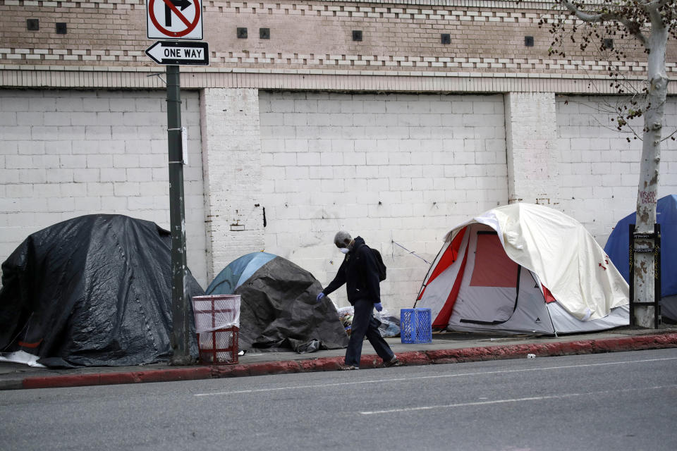 FILE - In this March 20, 2020, file photo, a man covers his face with a mask as he walks past tents on skid row in Los Angeles. The 9th U.S. Court of Appeals on Thursday, Sept. 23, 2021, overturned a federal judge’s sweeping order that required the city and county of Los Angeles to quickly find shelter for all homeless people living on downtown’s Skid Row. (AP Photo/Marcio Jose Sanchez, File)