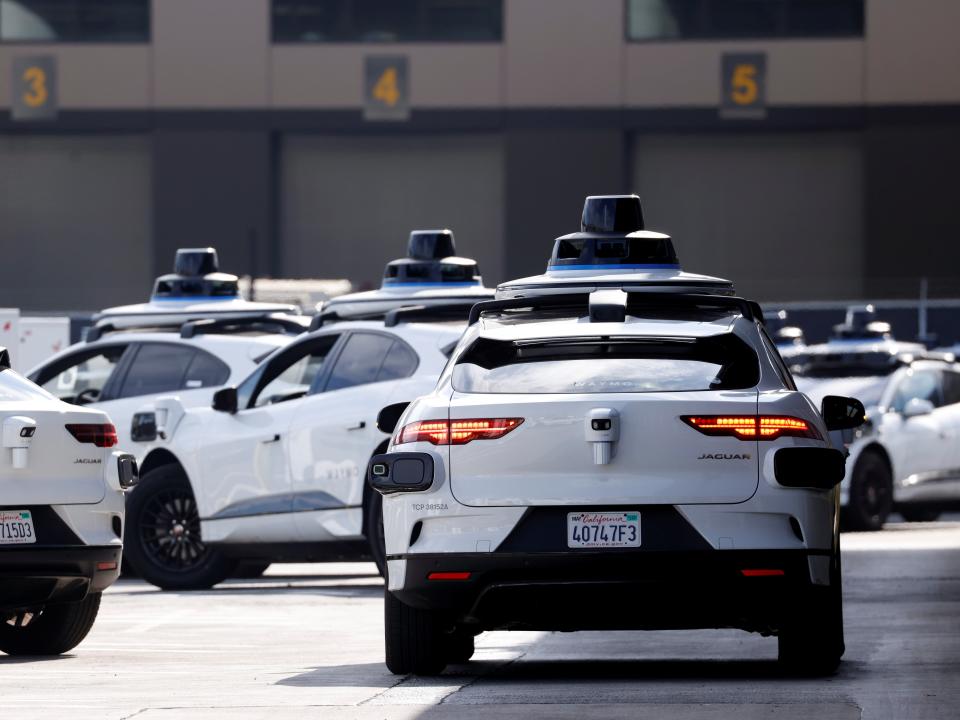 Several white Waymo autonomous cars are seen together on the street