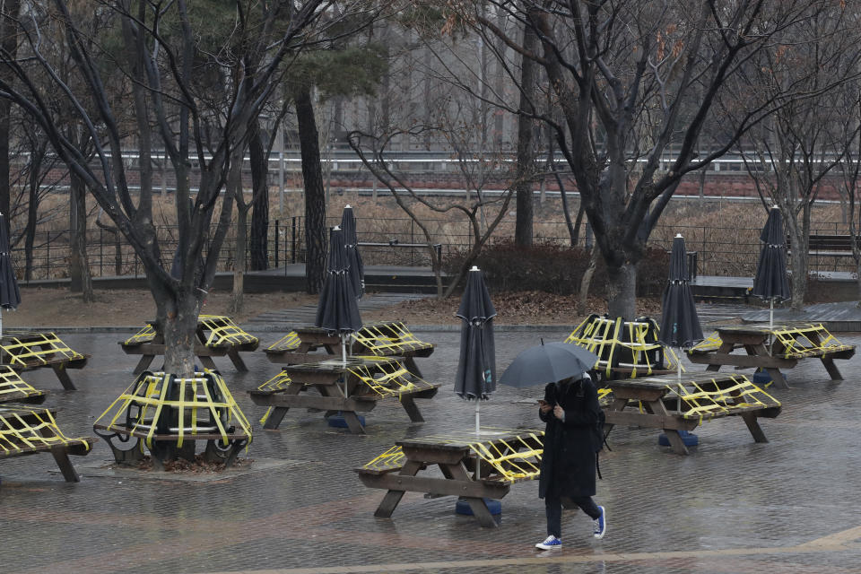 A man wearing a face mask as a precaution against the coronavirus walks past benches and tables taped for social distancing in Seoul, South Korea, Thursday, Jan. 21, 2021. (AP Photo/Lee Jin-man)