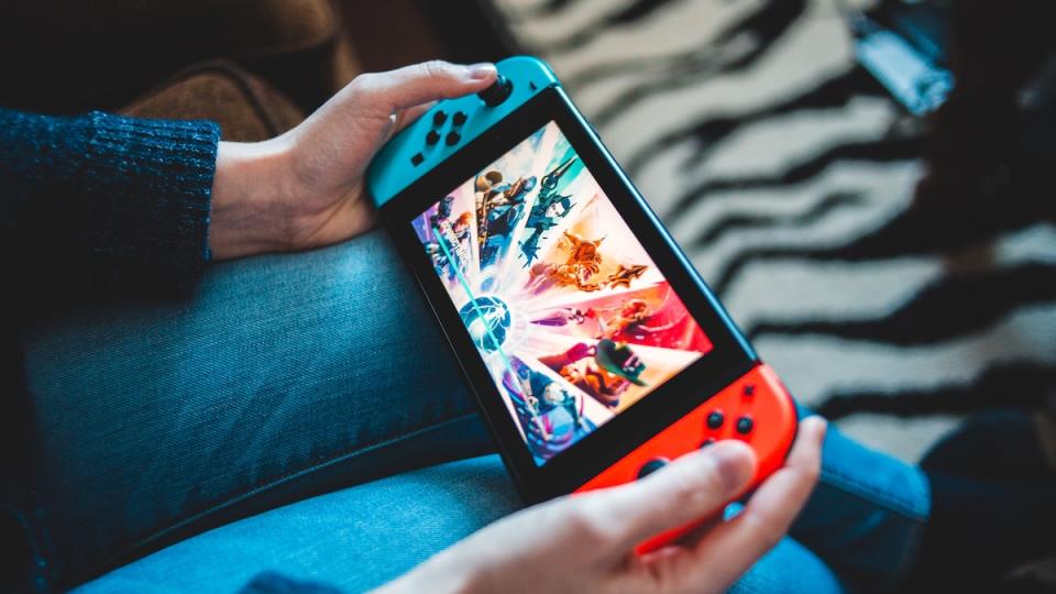 A person holds a Nintendo Switch with red and blue Joycons