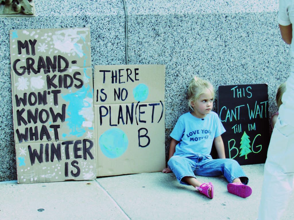 Child sits with signs at Milwaukee climate march