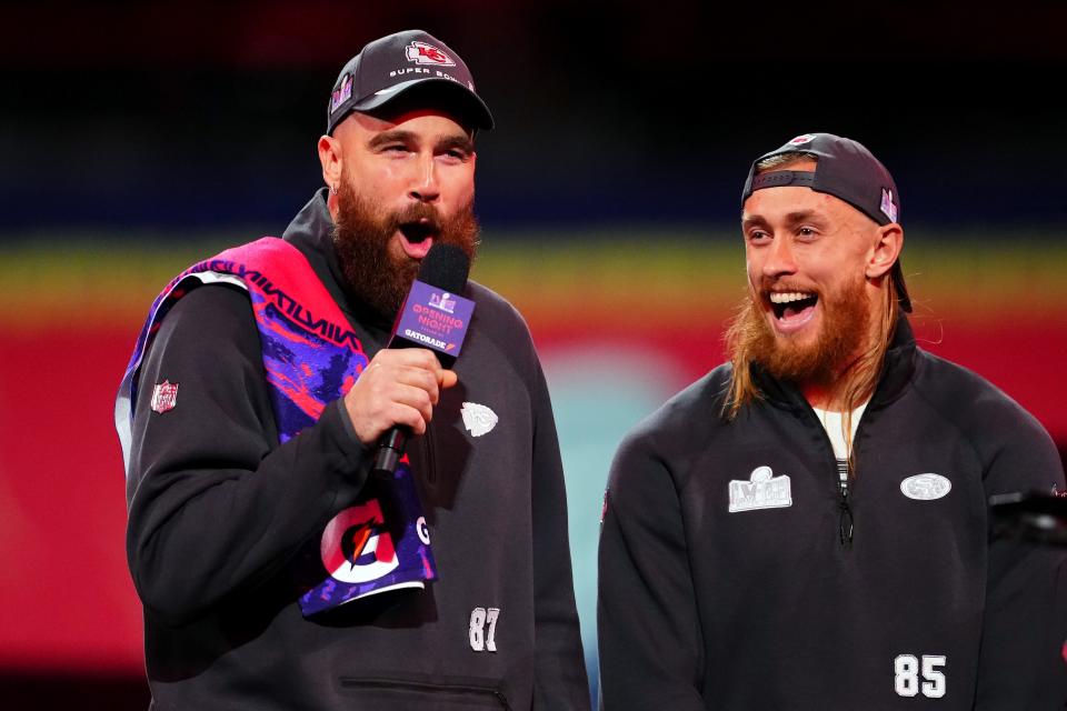 Travis Kelce of the Kansas City Chiefs (L) and George Kittle of the San Francisco 49ers stand on stage during Super Bowl LVIII Opening Night at Allegiant Stadium.