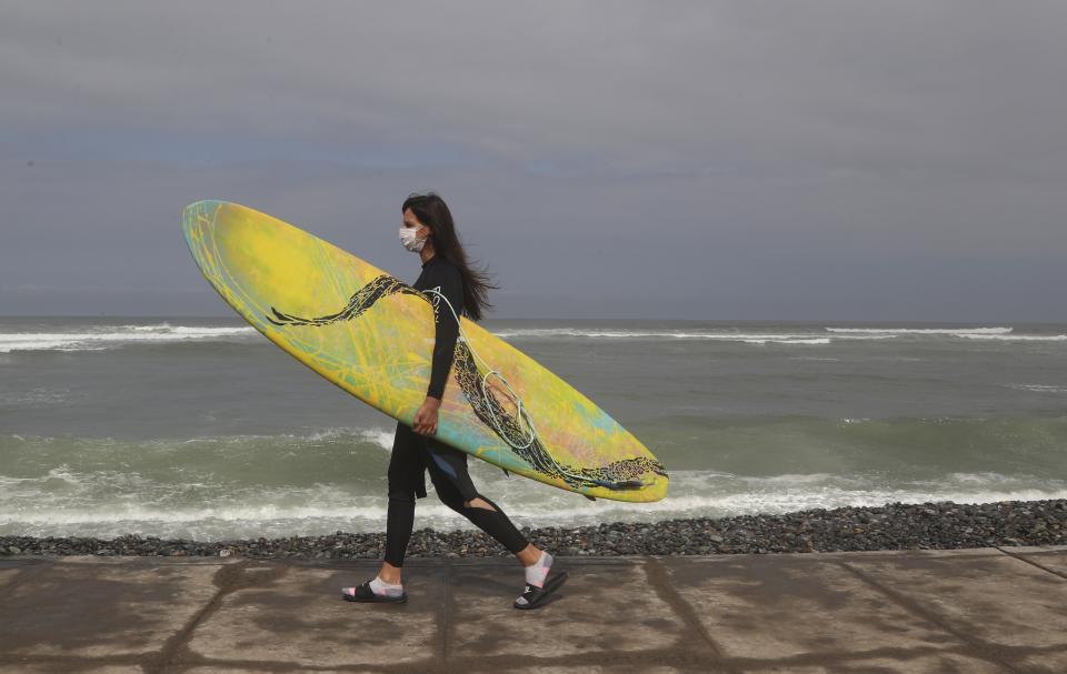 Wearing a face mask as a precaution amid the spread of the new coronavirus, a surfer walks to Waikiki beach in the Miraflores district of Lima, Peru, Thursday, June 11, 2020. The emblematic surfers who dot Peru's coastline are retaking to the waves as the hard-hit nation relaxes COVID-19 related restrictions on outdoor sports. (AP Photo/Martin Mejia)