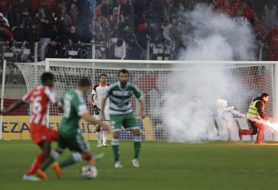 A security person removes a flare from Panathinaikos' goalkeeper Stefanos Kapino's area during a Greek League soccer match against Olympiakos at Georgios Karaiskakis stadium, in Piraeus port, near Athens, on Sunday, March 2, 2014. Olympiakos’ undefeated run is over after a 3-0 home defeat by Panathinaikos. Very little soccer was played in the last 12 minutes, as Olympiakos fans kept throwing flares and projectiles after they had a penalty awarded in their favor. (AP Photo/Thanassis Stavrakis)