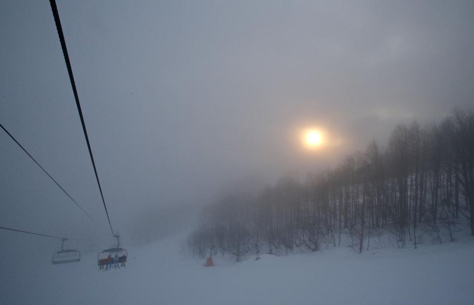 The sun tries to break through the heavy fog as skiers take a chair lift up the mountain near the alpine skiing training slopes at the Sochi 2014 Winter Olympics, Monday, Feb. 17, 2014, in Krasnaya Polyana, Russia. (AP Photo/Christophe Ena)