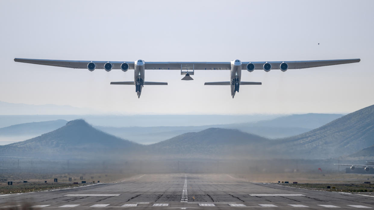  A dual-fuselage aircraft lifts off carrying a test vehicle. 