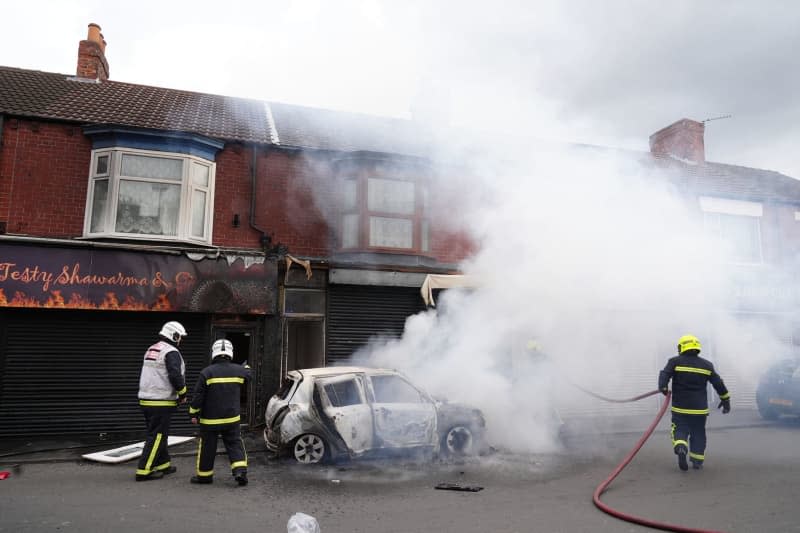 Firefighters extinguish a burning car on Parliament Road in Middlesbrough during an anti-immigration demonstration. After the knife attack on children in Southport on 29 July 2024, numerous nationalist and anti-Islamic protests inflame the mood in the UK. Owen Humphreys/PA Wire/dpa