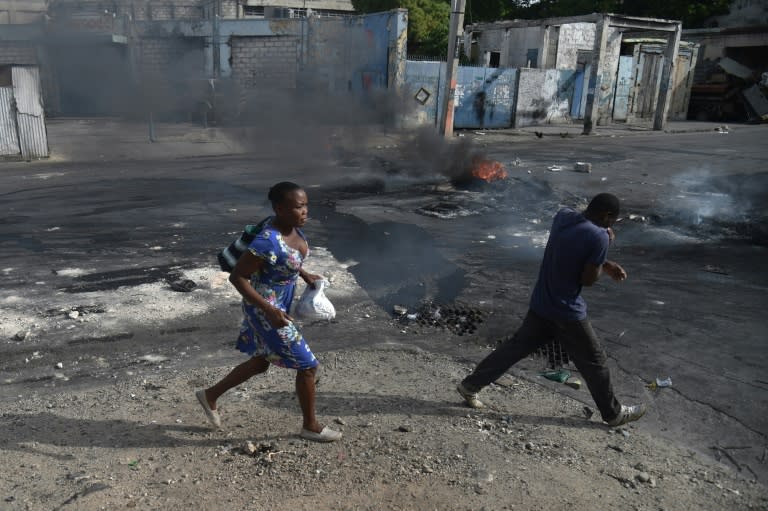 People walk past burning tires placed by protesters in the streets of Port-au-Prince