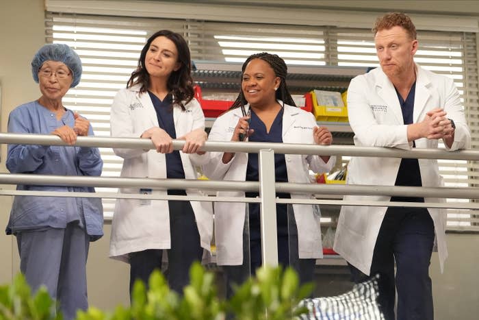 Four medical professionals standing by a railing on an upper floor of the hospital in a scene Grey's Anatomy